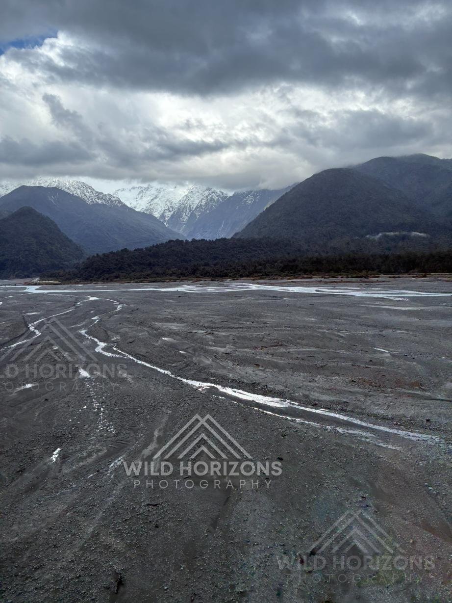 Wide alpine river flats beneath brooding mountain skies. Franz Josef, New Zealand