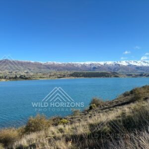 Clear alpine lake stretching beneath distant snow-lined ranges. Mackenzie Basin, New Zealand