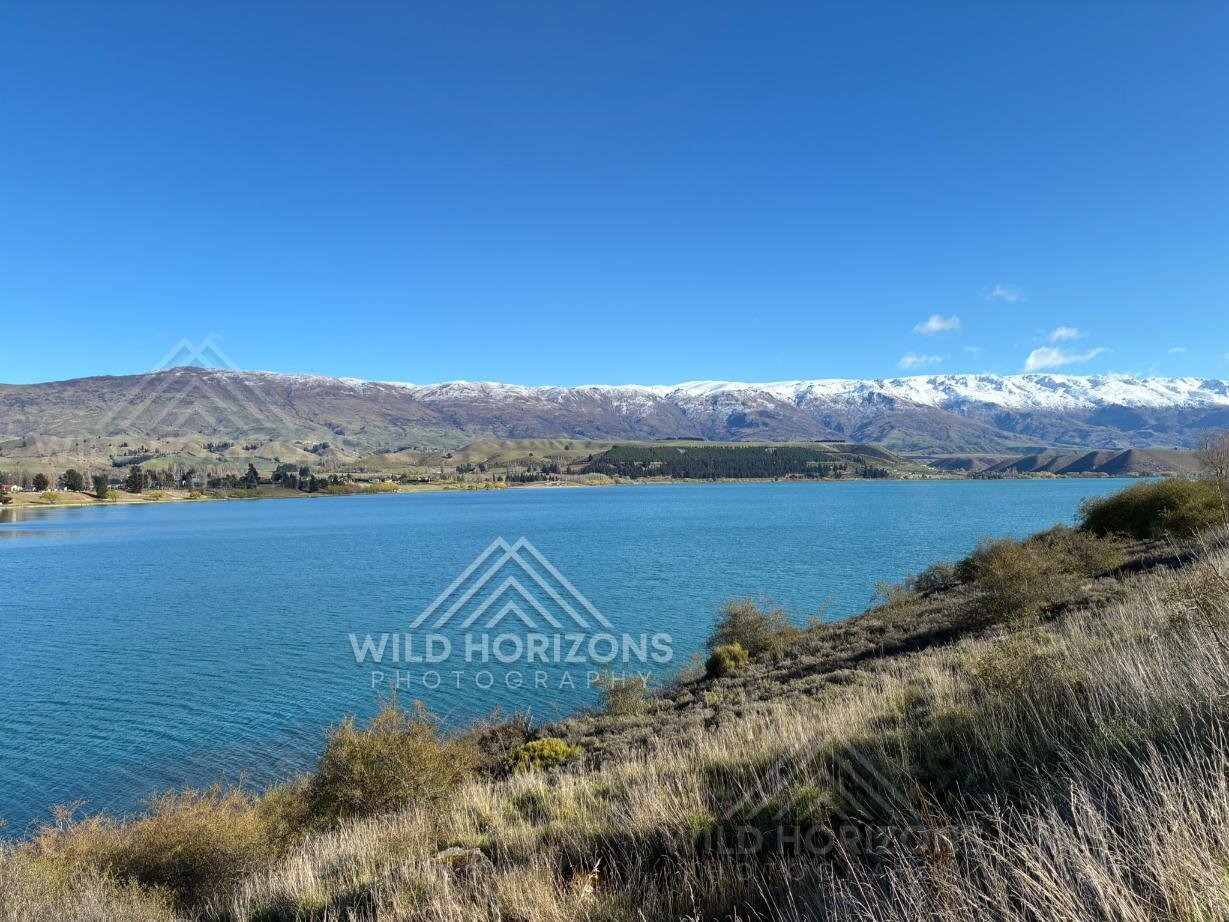 Clear alpine lake stretching beneath distant snow-lined ranges. Mackenzie Basin, New Zealand