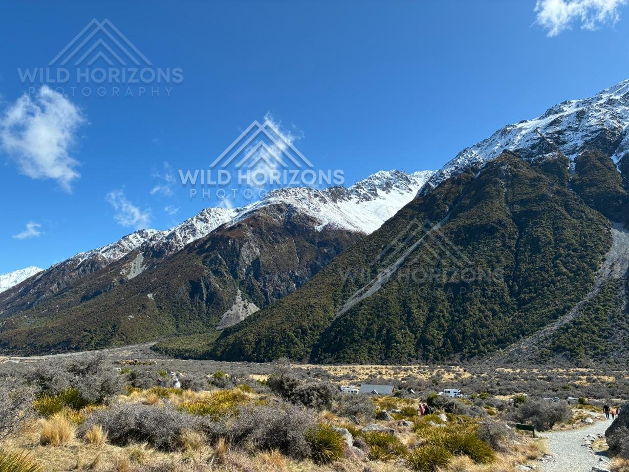 Alpine valley floor beneath steep snow-dusted mountain slopes. Aoraki / Mount Cook National Park, New Zealand