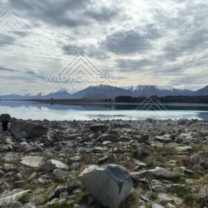 Rocky Lakeshore and Reflected Mountain Range under Overcast Skies. Lake Tekapo, New Zealand