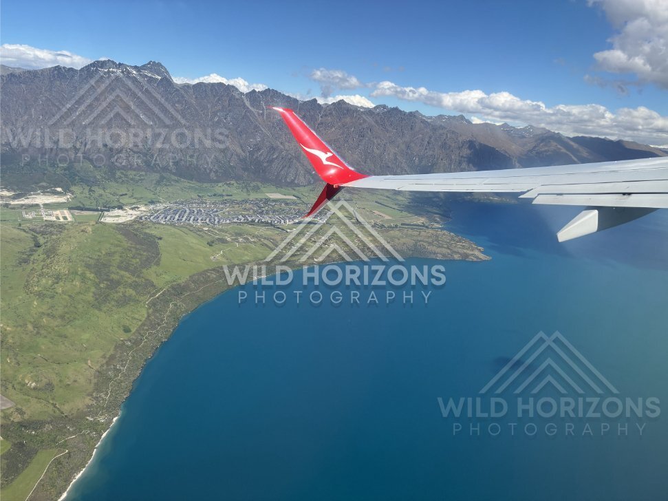 Aircraft wing frames an aerial view across Lake Wakatipu and Queenstown. Queenstown and Lake Wakatipu, New Zealand