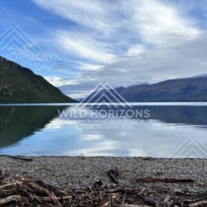 Wide view across the glassy waters of Lake Te Anau toward forested slopes and peaks. Lake Te Anau, New Zealand
