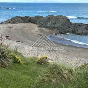 Small sheltered beach framed by dark volcanic rock and gentle ocean swell. Riverton coastline, New Zealand