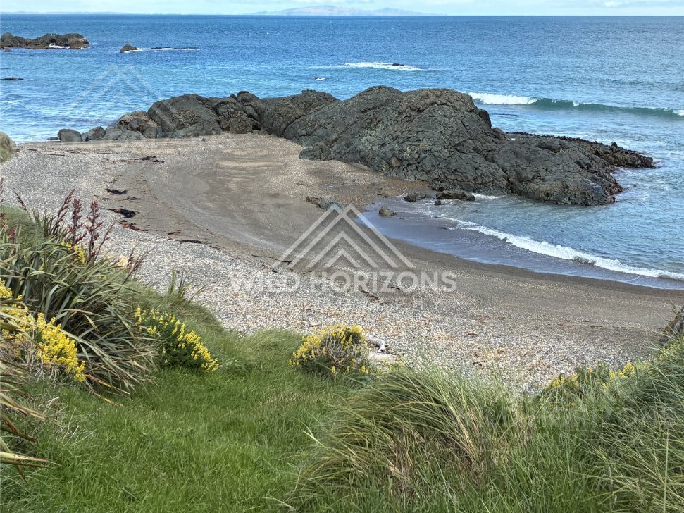 Small sheltered beach framed by dark volcanic rock and gentle ocean swell. Riverton coastline, New Zealand