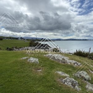 Grassy foreshore with scattered homes under dramatic cloud above calm coastal water. Riverton, New Zealand