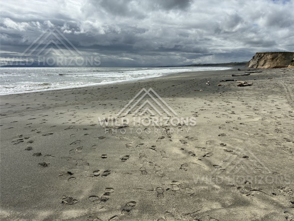 Empty stretch of black-sand shoreline with dramatic skies and distant cliffs. Southland coast, New Zealand