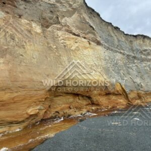 Eroded cliff face and dark sand revealing layered geology along the shoreline. Southland coast, New Zealand