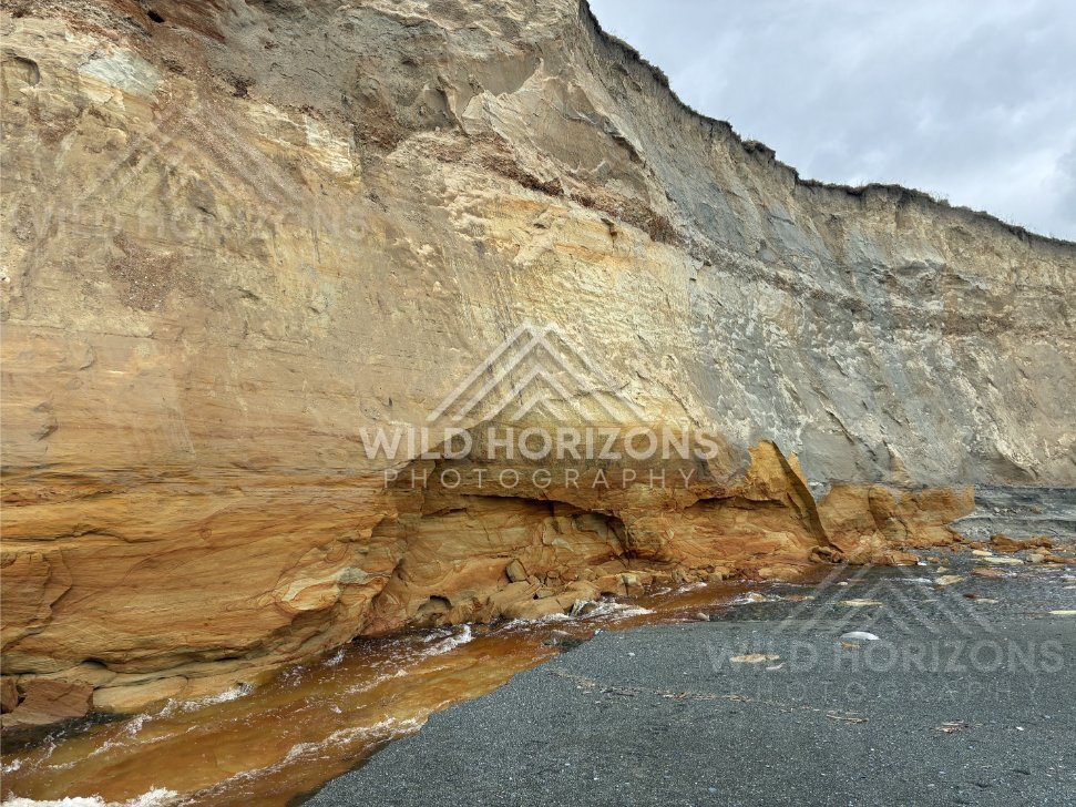 Eroded cliff face and dark sand revealing layered geology along the shoreline. Southland coast, New Zealand
