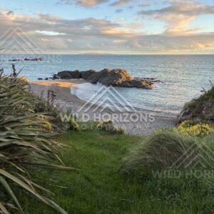 A Small Sandy Cove Curving Around Sunlit Rock Formations Under a Soft Evening Sky. Riverton, New Zealand