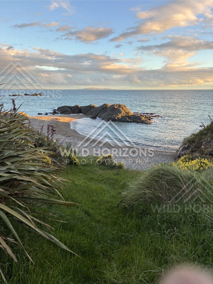 A Small Sandy Cove Curving Around Sunlit Rock Formations Under a Soft Evening Sky. Riverton, New Zealand