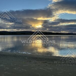 Golden sunset reflecting across still lagoon and wet sand. Surat Bay, New Zealand