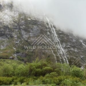 Braided waterfall spilling from low cloud on Milford Road, New Zealand