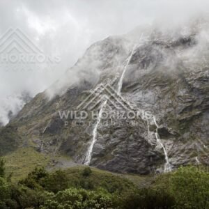 Waterfalls and mist across Fiordland rock walls on Milford Road, New Zealand