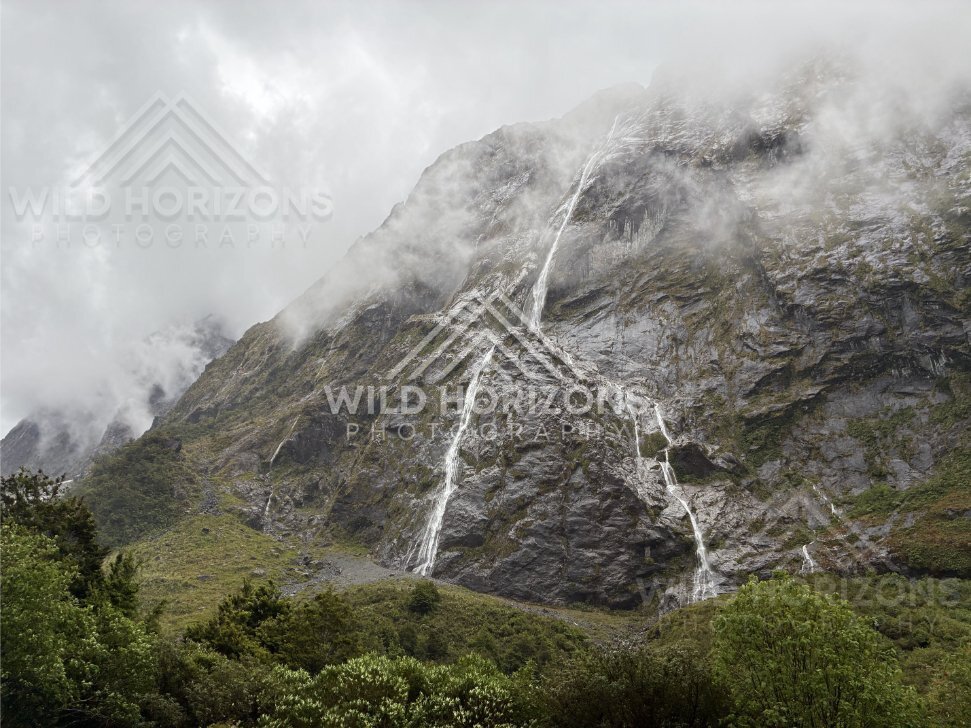Waterfalls and mist across Fiordland rock walls on Milford Road, New Zealand