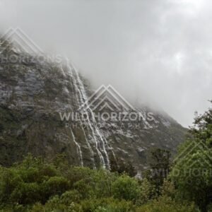 Curtain of water down Fiordland cliff under fog on Milford Road, New Zealand