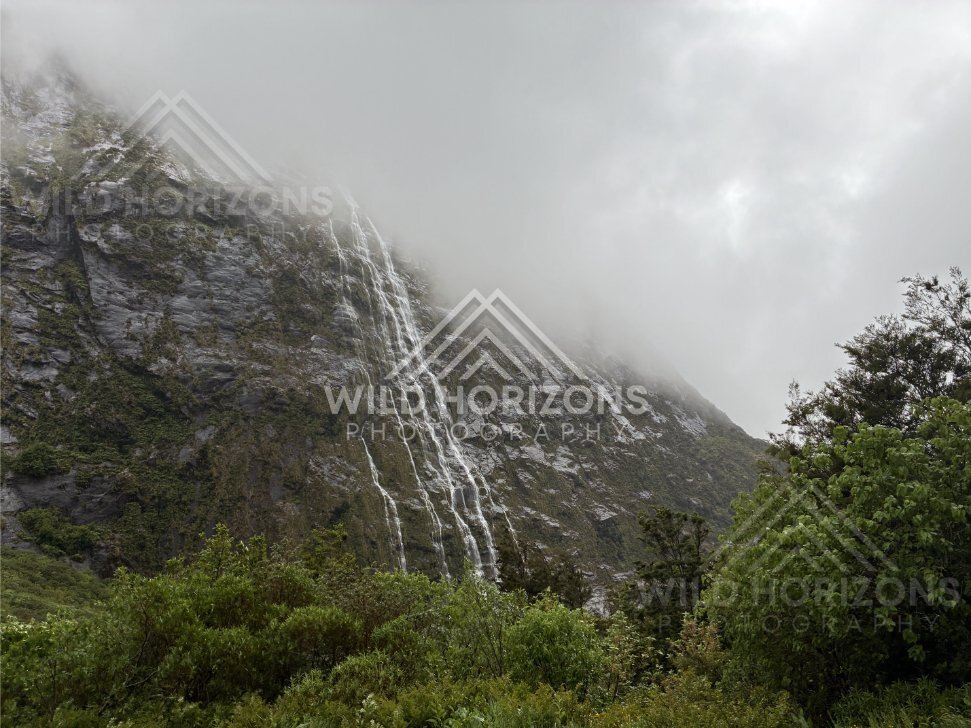 Curtain of water down Fiordland cliff under fog on Milford Road, New Zealand