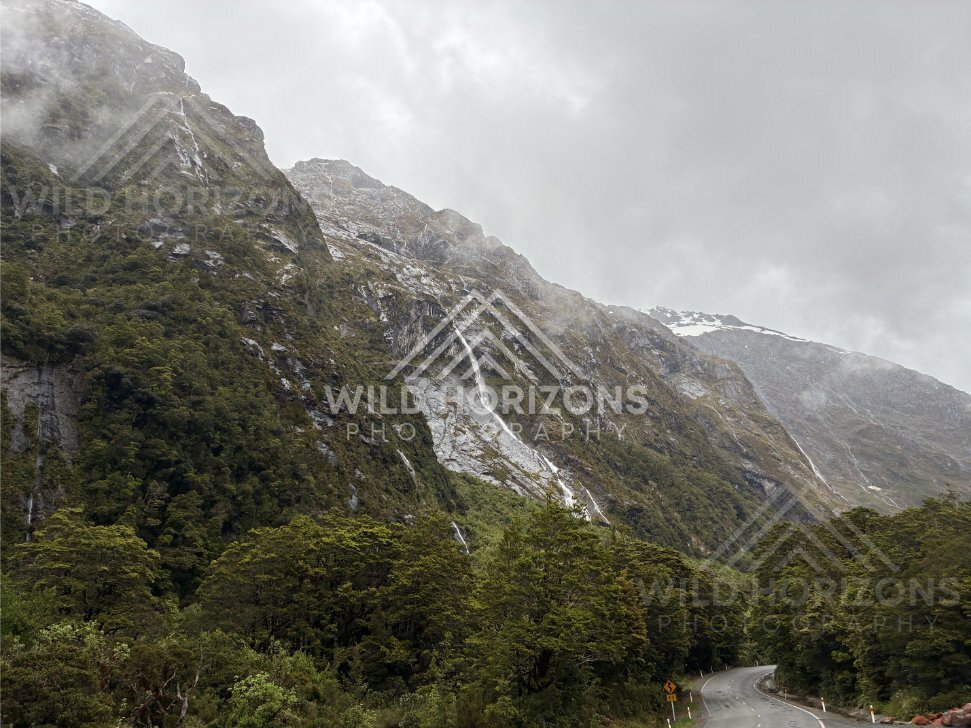 Winding mountain road beneath waterfalls on Milford Road, New Zealand