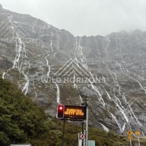 Waterfall-covered cliff beside roadworks on Milford Road, New Zealand