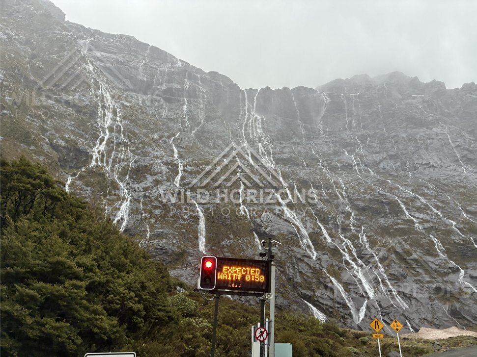 Waterfall-covered cliff beside roadworks on Milford Road, New Zealand