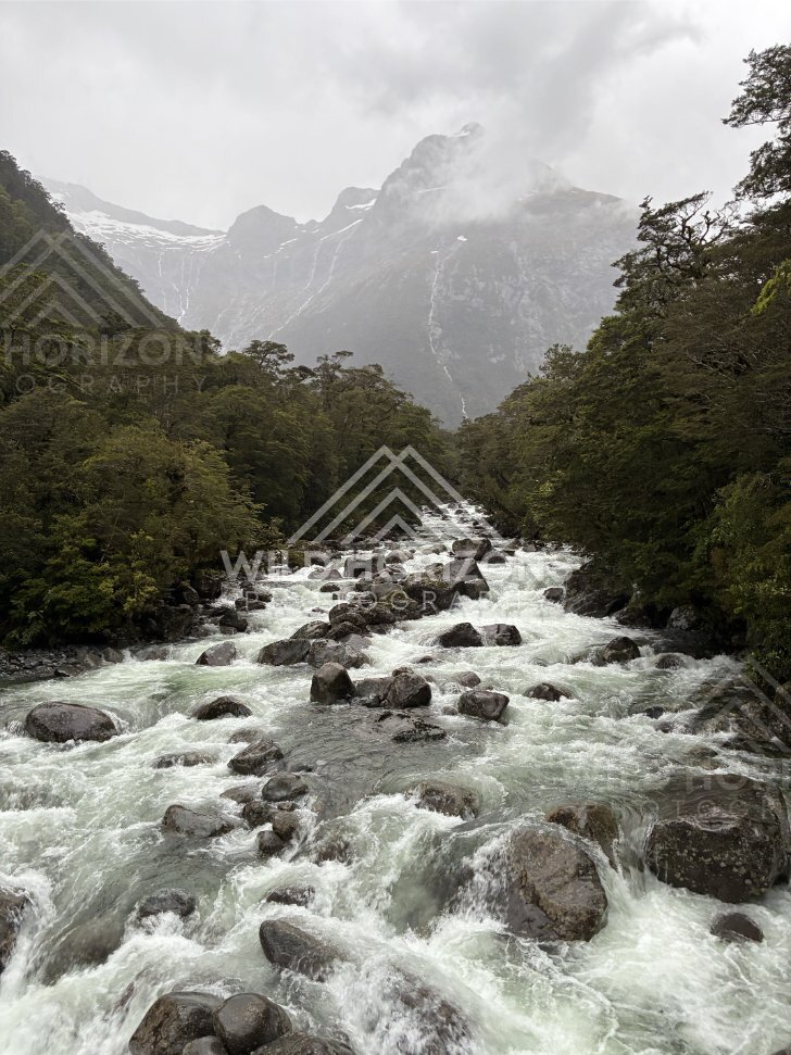 Boulder-strewn river rapids beneath misty peaks, Milford Road, New Zealand