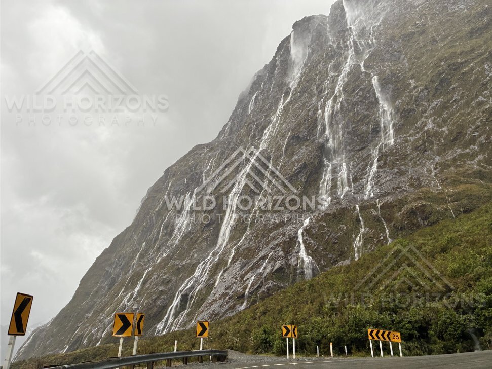 Roadside curve signs below cascading Fiordland waterfalls, Milford Road, New Zealand