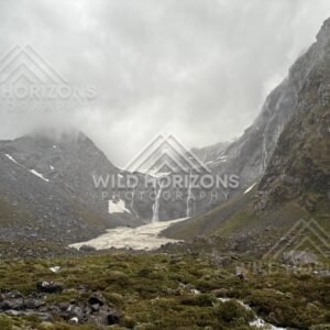 Alpine basin with snowfield and distant waterfall, Milford Road, New Zealand