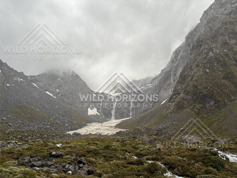 Alpine basin with snowfield and distant waterfall, Milford Road, New Zealand