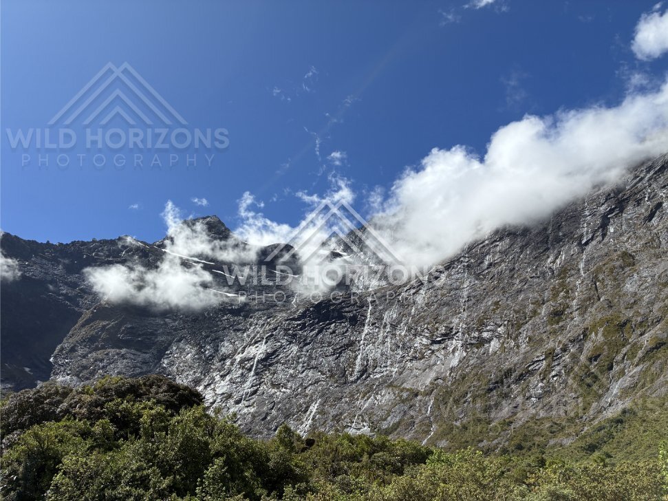 Sunlit Rock Face with Misty Cloud and Waterfall Threads, Milford Road, New Zealand