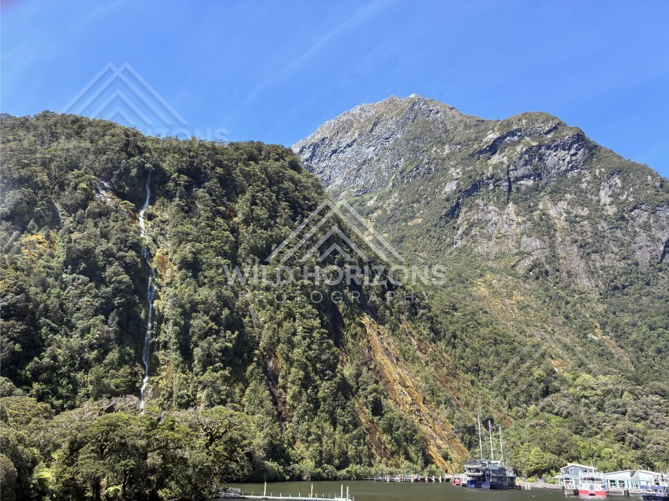 Waterfall above Milford Sound wharf and boats, New Zealand