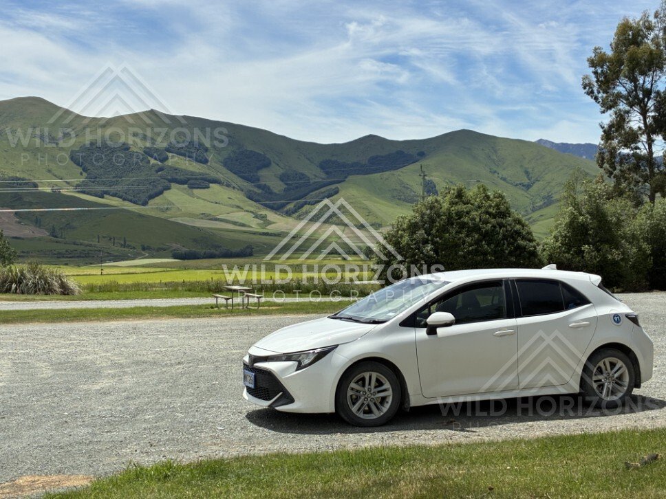 Roadside verge with parked car and hills beyond. Rural Southland, New Zealand.