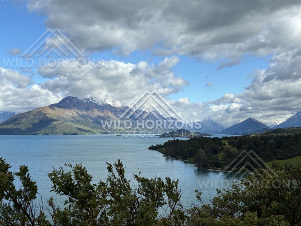 Mountain lake framed by native shrubs and distant peaks. Glenorchy, New Zealand.