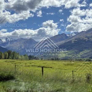 Green pasture with mountain range under scattered cloud. Glenorchy, New Zealand.