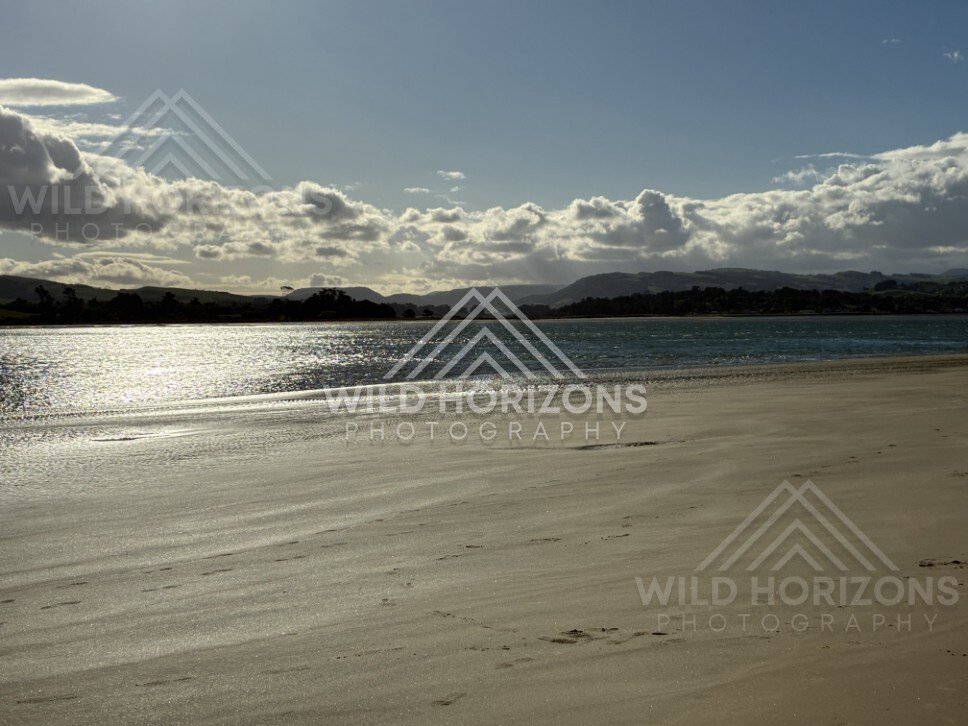 Wide sandy beach with reflective wet sand. Surat Bay, New Zealand.