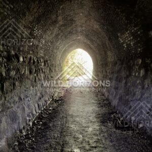 Stone-lined tunnel with light at far end. Tunnel Hill, New Zealand.
