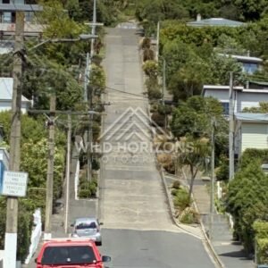Steep residential street with houses and parked car. Dunedin, New Zealand.