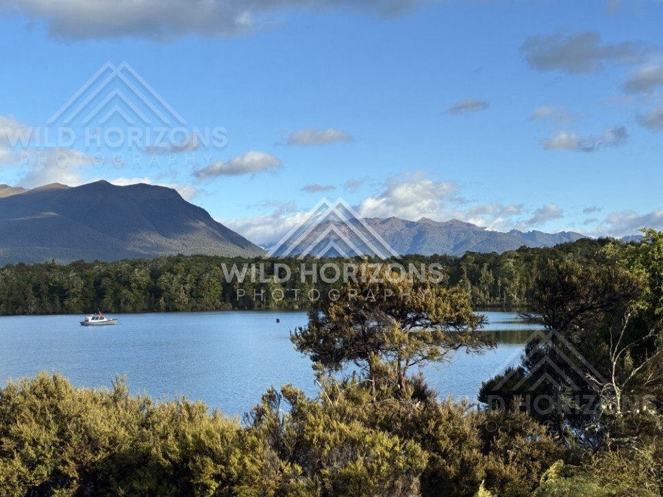 Small Boat on a Calm Fiordland Lake with Mountains Beyond. Milford Road, New Zealand.