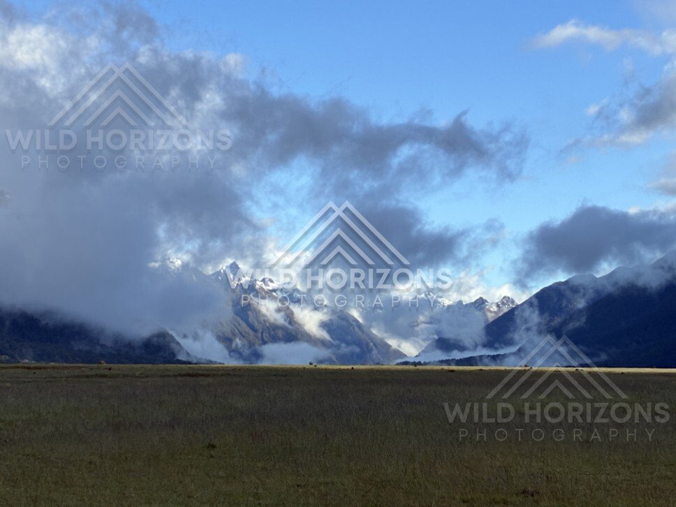 Snowy Fiordland Peaks Under Dark Cloud Above Plains. Milford Road, New Zealand.