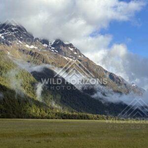 Sunlit Peak and Hanging Cloud Above the Valley Floor. Milford Road, New Zealand.