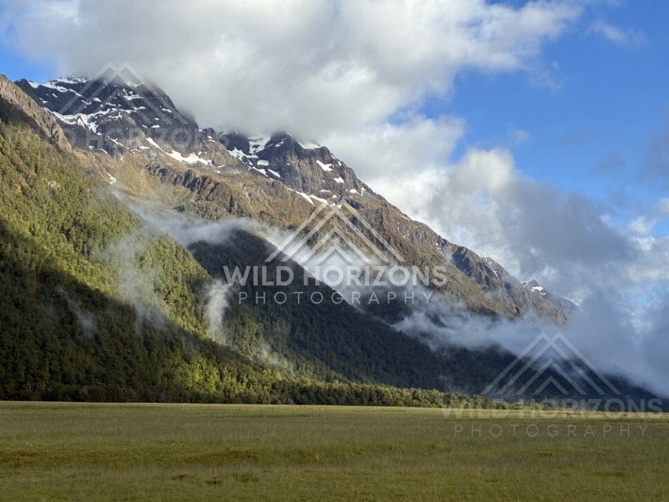 Sunlit Peak and Hanging Cloud Above the Valley Floor. Milford Road, New Zealand.