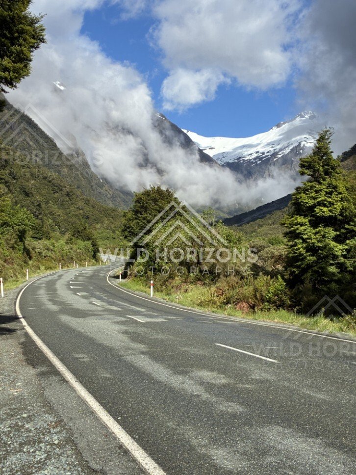 Milford Road Curve Through Forest Toward Cloud-Wrapped Mountains. Milford Road, New Zealand.