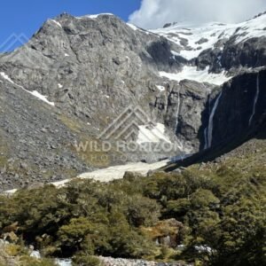 Rocky Alpine Basin with Snowfields and Tall Waterfall. Milford Road, New Zealand.