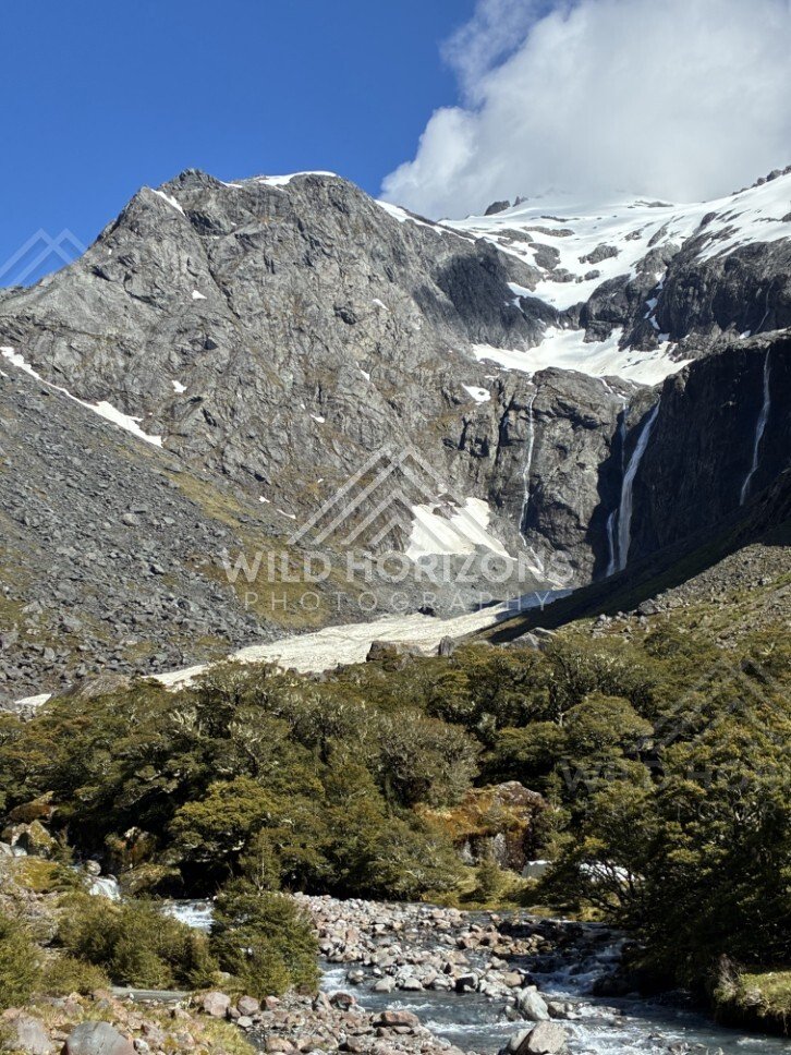 Rocky Alpine Basin with Snowfields and Tall Waterfall. Milford Road, New Zealand.