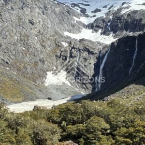 Twin Waterfalls Dropping Beside Snowfields in a Rocky Basin. Milford Road, New Zealand.