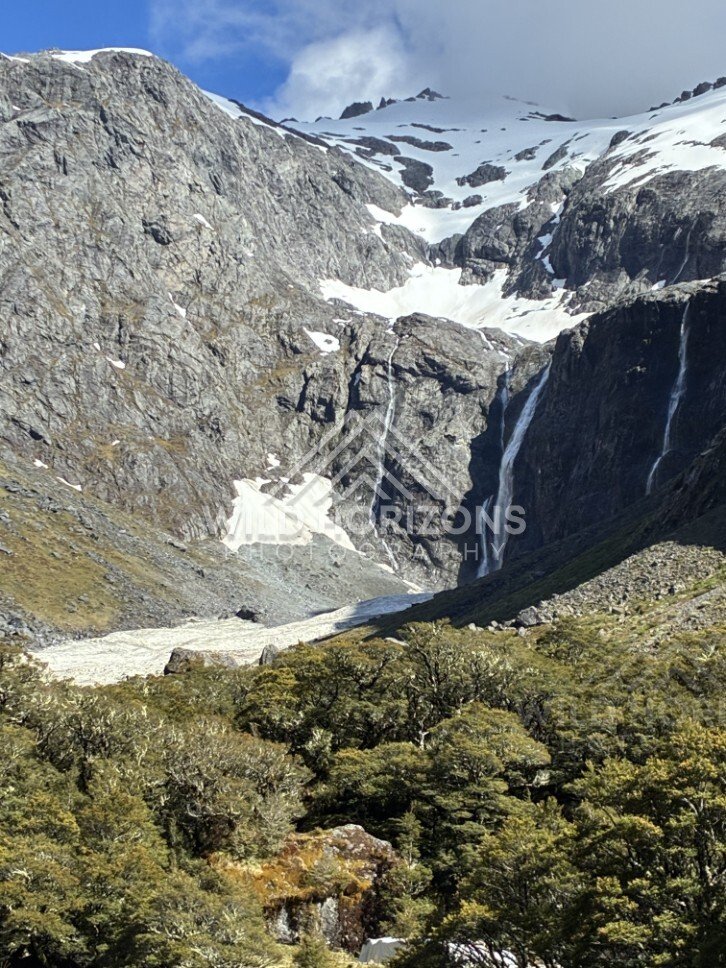Twin Waterfalls Dropping Beside Snowfields in a Rocky Basin. Milford Road, New Zealand.