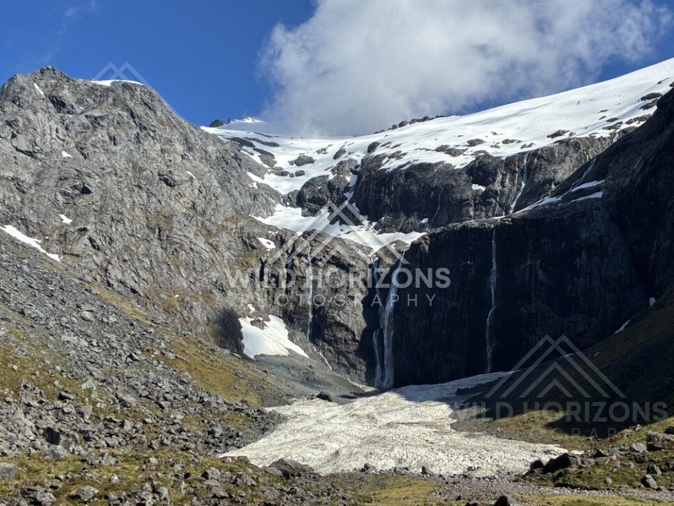 Waterfall Dropping into a Snow-Filled Alpine Basin Under Cloud. Milford Road, New Zealand.