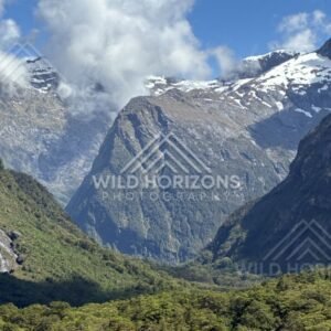 Snow-Capped Mountains Framing a Green Valley Under Towering Clouds. Milford Road, New Zealand.