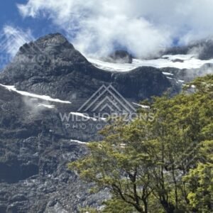 Snow-Powdered Ridge and Dark Rock Face Above Forest Canopy. Milford Road, New Zealand.