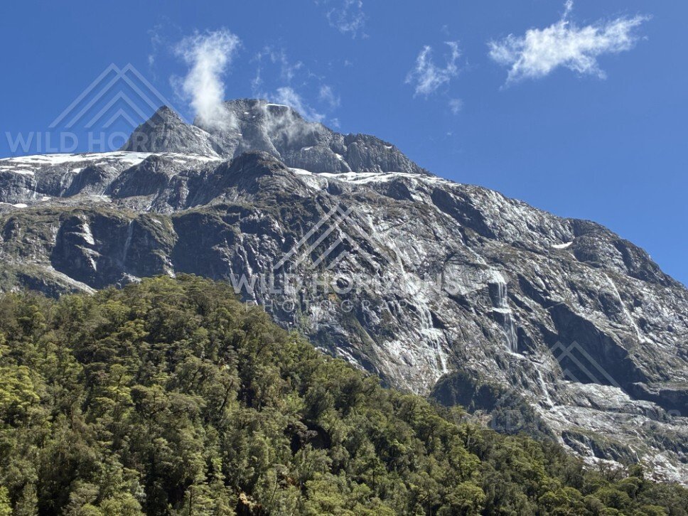 Massive Mountain Wall with Waterfalls and Forested Foothills. Milford Road, New Zealand.