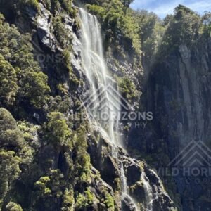 Sunlit Waterfall Cascading Over Dark Rock Ledges. Milford Sound, New Zealand.
